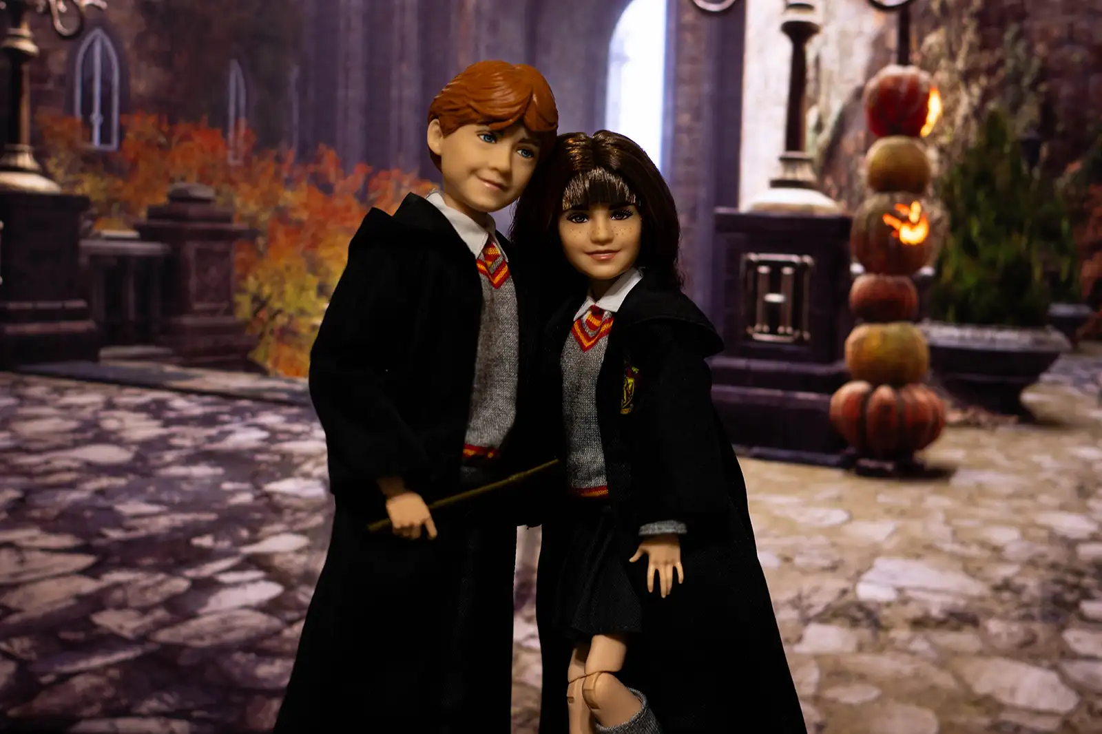 Mattel Ron Weasley and Hermione Granger dolls in a Halloween-decorated Hogwarts courtyard